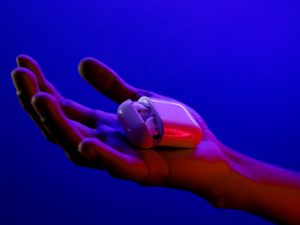 A pair of earphones/earbuds in someones hands with a blue light in the background
